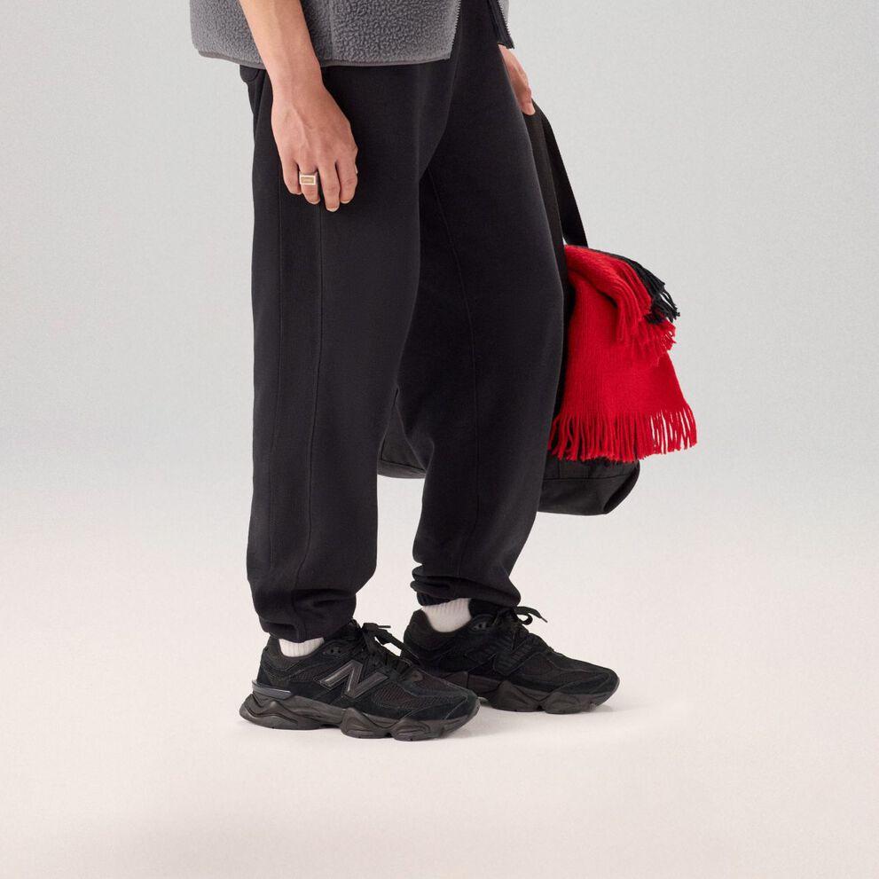 Jeune homme en pantalon noir et chaussures debout sur un fond gris.